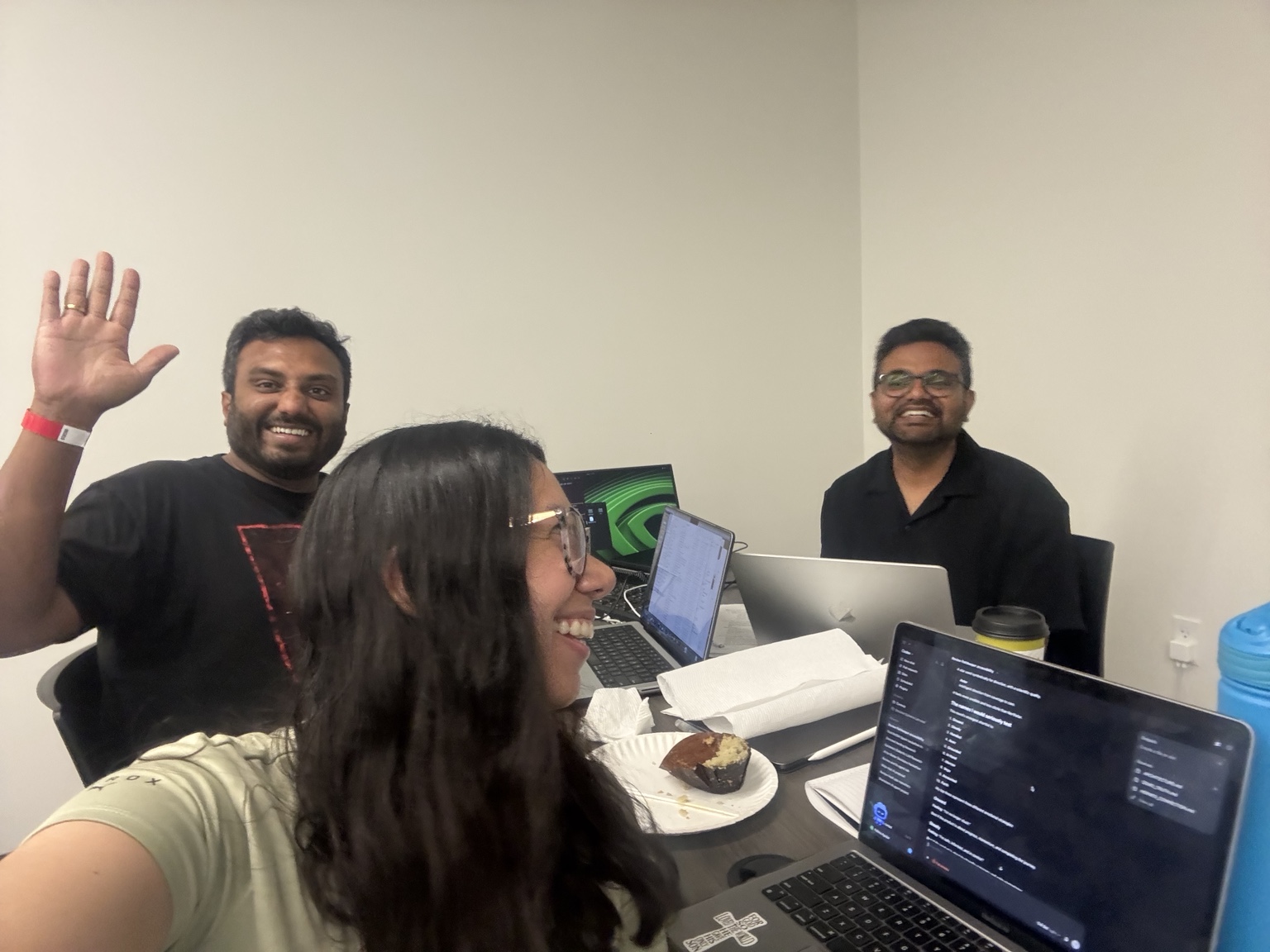 The VELA team at the same table, one member waving, laptops showing the working system.