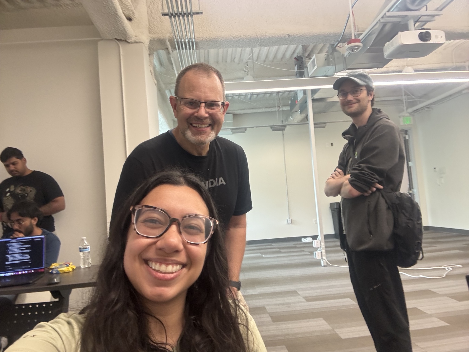 Team member on the hackathon build floor with mentors and other participants in the background.
